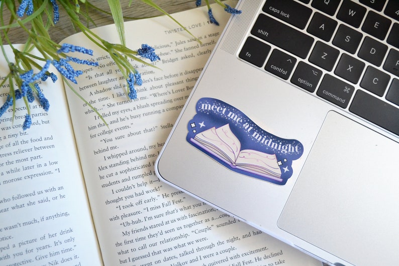 May include: A blue and purple sticker with a book and stars on a laptop. The sticker says "Meet me at midnight".