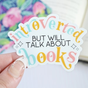 May include: A white sticker with the text "introverted but will talk about books" in colorful letters. The sticker has a pink, yellow, and blue color scheme.