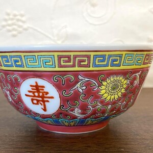 May include: A decorative ceramic bowl with a red background and intricate floral and geometric patterns. The bowl features a white rim and a red base. A Chinese character is displayed on the side of the bowl.