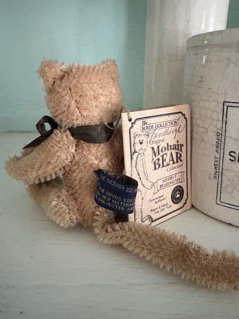 Pu&ograve; includere: Un orsacchiotto vintage in mohair marrone di The Boyd's Collection, con un nastro scuro e un'etichetta. L'etichetta recita "Original Mohair Bear Collection" e "Adams F. Bearington". L'orso &egrave; realizzato in nuovo materiale, poliestere e ha un'etichetta blu.