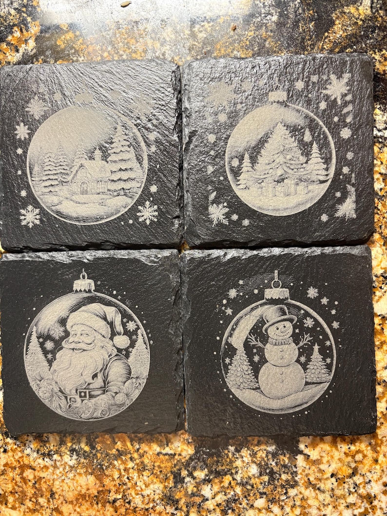 Pode incluir: Conjunto de quatro bases quadradas de ard&oacute;sia preta. Cada base apresenta uma cena de inverno gravada diferente dentro de uma forma de enfeite de Natal. As cenas incluem uma casa, &aacute;rvores, Papai Noel e um boneco de neve.