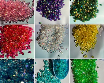 May include: Assortment of iridescent glass gems in various colors, including pink, red, clear, green, blue, and yellow. The gems are small and have a faceted, diamond-like appearance.