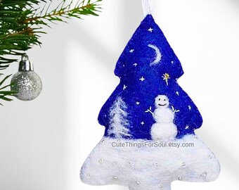 May include: A felt Christmas tree ornament in a deep blue color featuring a white snowman, a white pine tree, a crescent moon, and small stars. The base is covered in white felt with silver accents and the text CuteThingsForSoul.etsy.com.