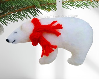 May include: A white felt polar bear ornament featuring a bright red knitted scarf wrapped around its neck. The bear has a black stitched nose and closed eyes. The text CuteThingsForSoul.etsy.com is visible above the bear's back.