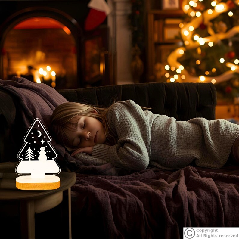 May include: A Christmas tree-shaped night light with a wooden base, featuring a white silhouette of a snowman, a pine tree, a crescent moon, and stars against a black background, emitting a soft glow from the bottom section.