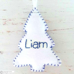 May include: A white felt Christmas tree ornament featuring a blue stitched border and the name Liam embroidered in blue thread across the center. A small white ribbon loop is attached to the top for hanging purposes.