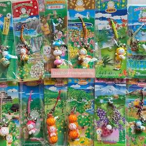 May include: A selection of Doraemon character keychains. Each keychain features a different design, including Doraemon figures, mushrooms, and other themed elements. The keychains are attached to colourful cords and hang from printed cards with Japanese text.