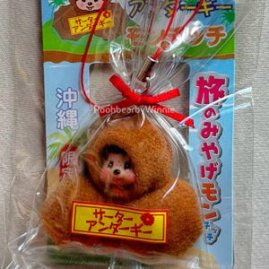 May include: A brown plush toy in a clear plastic bag tied with a red ribbon. The toy has a face and is labeled with Japanese text. The packaging includes additional Japanese text and a graphic of a tree.