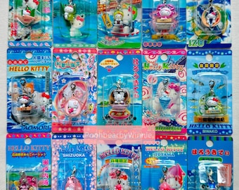 以下が含まれることがあります： 様々なデザインのハローキティのキーホルダーのコレクション。それぞれ透明なプラスチックケースに入っており、日本語のテキストが記載されています。キーホルダーは、鮮やかな色と詳細なデザインで、さまざまな設定のハローキティを特徴としています。