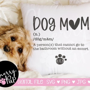 Può includere: Un cuscino bianco con il testo "Dog Mom" in corsivo nero. Il testo è definito come "(n.) /dôg/mäm/ Una persona(s) che non può andare in bagno senza scorta." Un'impronta di zampa nera si trova sotto il testo. Un piccolo cane marrone è sdraiato su una coperta bianca sullo sfondo.