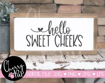 May include: A white wooden sign with a brown frame, featuring the text "hello sweet cheeks" in black lettering with a small heart above the word "hello".