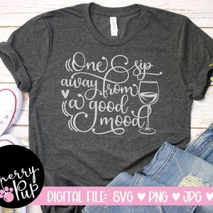 May include: A dark grey t-shirt with the text "One sip away from a good mood" in white lettering. A glass of wine is depicted next to the text.