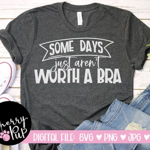 May include: A gray t-shirt with the text "SOME DAYS just aren't WORTH A BRA" in white. The shirt is on a white wooden surface with a pair of white sneakers and blue jeans.