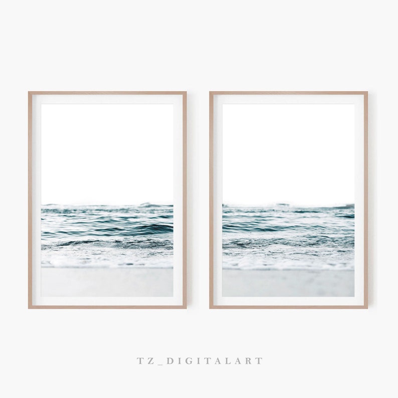 May include: Two framed prints of a beach scene with blue ocean waves crashing on the shore. The prints are in a light wood frame and are hung on a white wall.