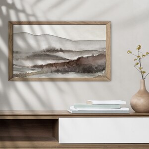 May include: A framed watercolor painting of a landscape with brown and gray hills and a wooden shelf with a stack of books and a vase with yellow flowers.