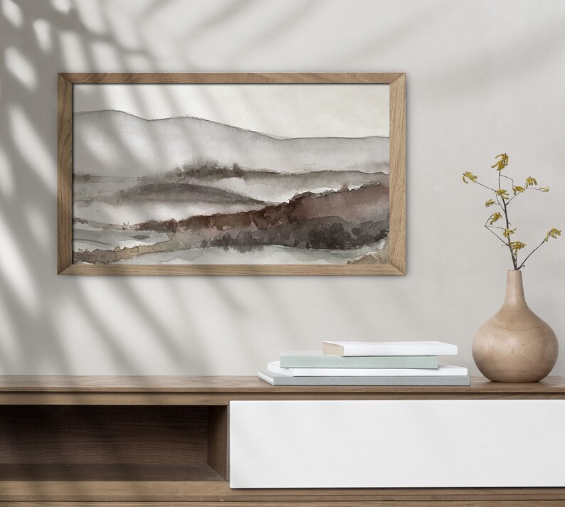 May include: A framed watercolor painting of a landscape with brown and gray hills and a wooden shelf with a stack of books and a vase with yellow flowers.