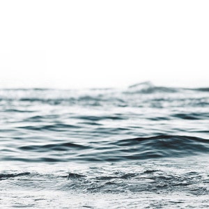 May include: A close-up of the surface of the ocean with small waves lapping at the shore. The water is a deep blue color and the background is a soft white.