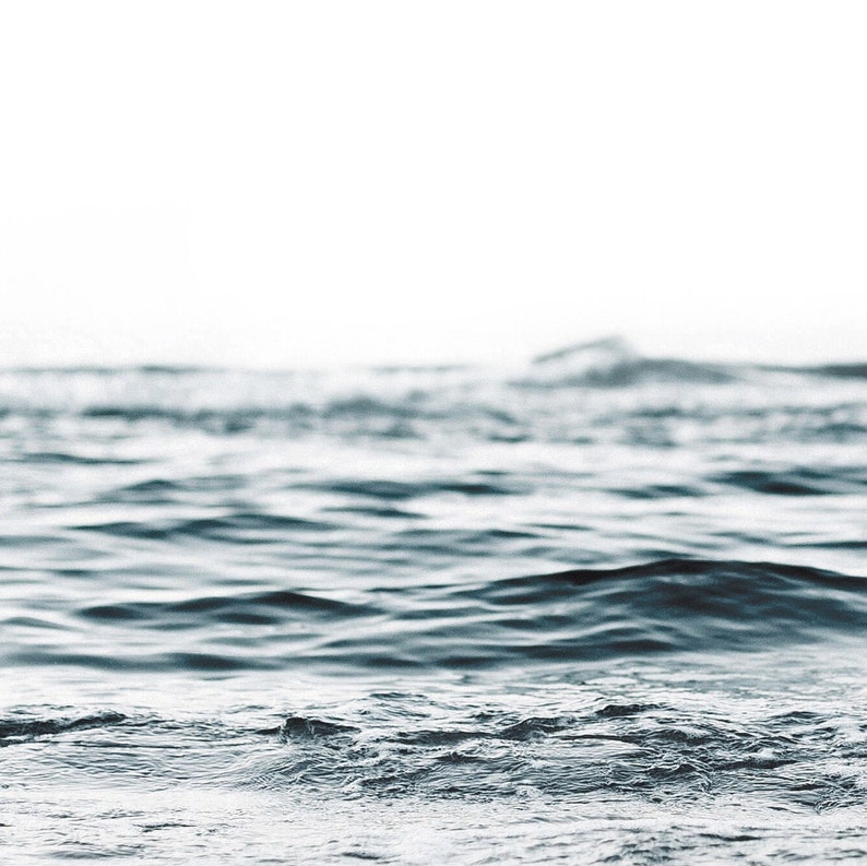 May include: A close-up of the surface of the ocean with small waves lapping at the shore. The water is a deep blue color and the background is a soft white.