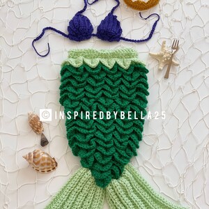 May include: A green and light green crocheted mermaid tail costume with a purple crocheted bikini top and a gold crocheted crown. The costume is laid out on a white background with seashells and a starfish.