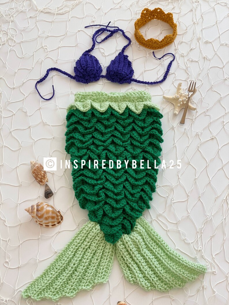 May include: A green and light green crocheted mermaid tail costume with a purple crocheted bikini top and a gold crocheted crown. The costume is laid out on a white background with seashells and a starfish.