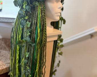 May include: A headpiece featuring long, multi-tonal green yarn dreadlocks adorned with artificial ivy vines, bright pink flowers, and orange blossoms. The yarn strands vary in shades of olive, lime, and forest green, creating a textured, layered look.