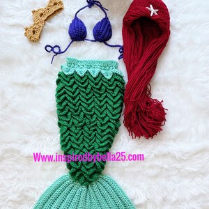 May include: A crocheted mermaid costume set for a baby, featuring a green and blue tail, a purple flower headband, a red wig with a white star, and a blue bikini top.