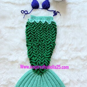 May include: A green and blue crocheted mermaid tail costume with a purple crocheted bikini top and a purple flower headband. The costume is on a white fluffy surface. www.inspiredbybella25.com
