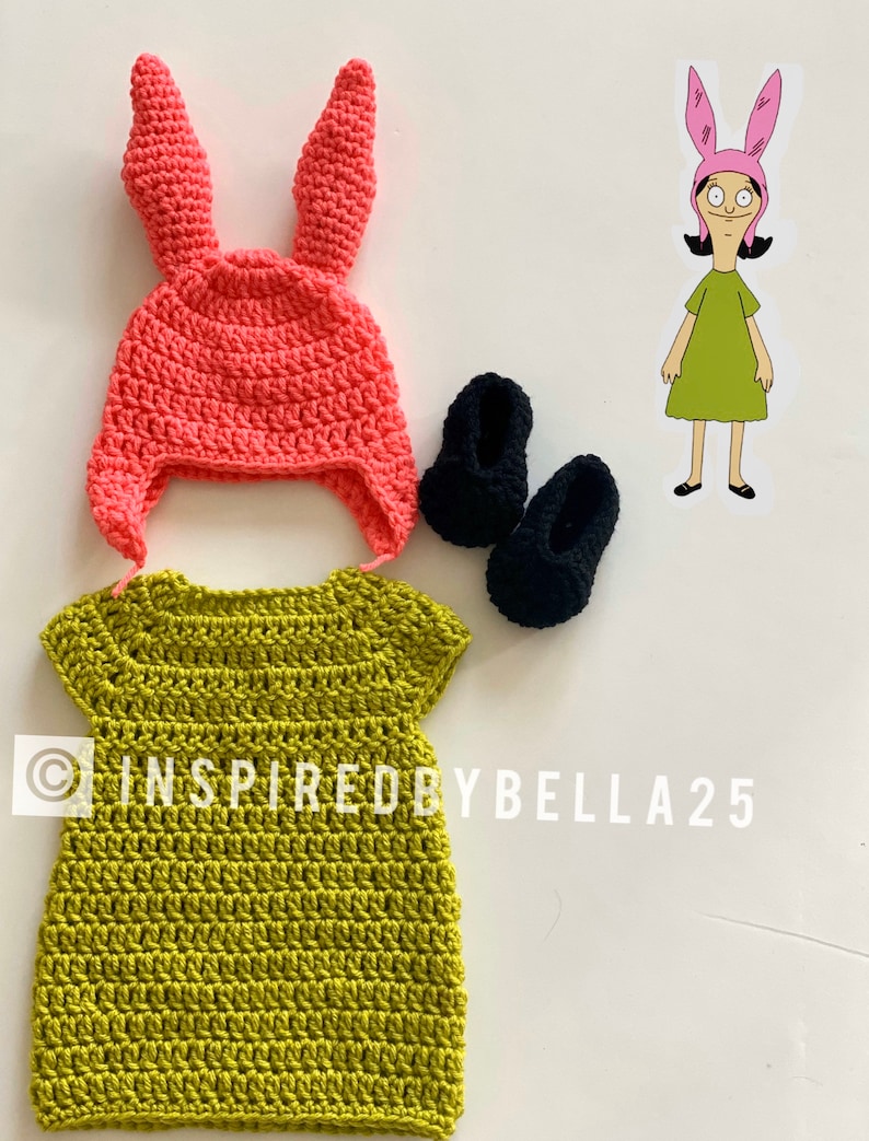 May include: A crocheted green dress with short sleeves, a pink crocheted bunny hat with long ears, and two black crocheted shoes. The image includes the text "INSPIRED BY BELLA 25".