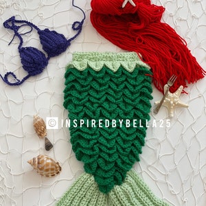 May include: A green crocheted mermaid tail with a light green tail fin. A purple crocheted bikini top and a red crocheted hat with a white starfish are also included. The image is on a white background with a white fishing net.