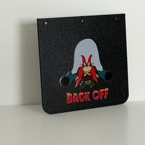May include: Black rectangular sign featuring a cartoon character with a red beard and the text "BACK OFF" in red and orange. The sign has three holes at the top and two circular holes near the bottom.