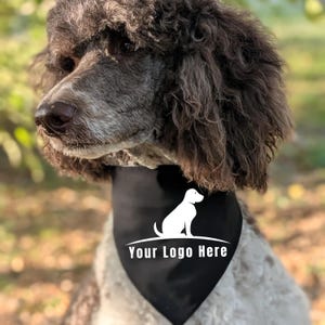May include: A black triangular pet bandana featuring a white graphic of a sitting dog silhouette above the text Your Logo Here. The bandana is worn around the neck of a brown and white curly-haired dog with dark eyes and a dark nose.