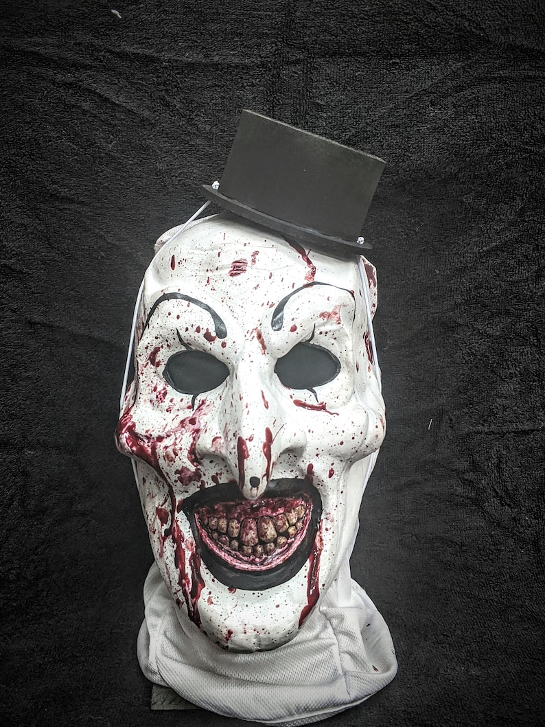 May include: A white creepy clown mask with a black top hat, splattered with red paint, and a wide, toothy grin.