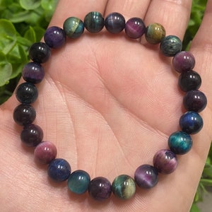 May include: A bracelet made of round, multi-colored beads. The beads are a mix of dark blue, green, purple, and gold.