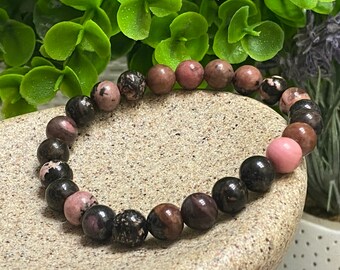 May include: A pink and black gemstone bracelet with round beads. The bracelet is made of natural stones and is a beautiful and unique piece of jewelry.