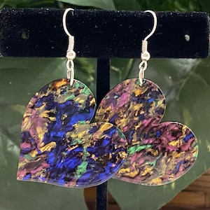 May include: A pair of heart-shaped earrings with a colorful abstract design. The earrings are made of resin and have a silver hook.
