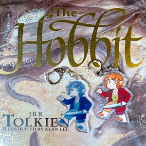 K&ouml;nnte beinhalten: Zwei Schl&uuml;sselanh&auml;nger mit Figuren aus "Der Hobbit" von J.R.R. Tolkien. Die Figuren sind ein blau gekleideter Elf mit einem Schwert und ein rot gekleideter Hobbit mit einem Schwert.