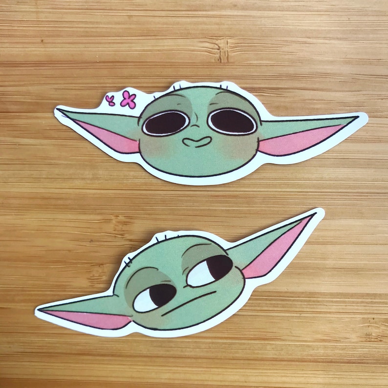 K&ouml;nnte beinhalten: Zwei Aufkleber mit einem gr&uuml;nen Alien-Charakter mit gro&szlig;en Augen. Der erste Aufkleber hat eine rosa Blume auf dem Kopf und das Alien l&auml;chelt. Der zweite Aufkleber zeigt das Alien, das mit neutralem Gesichtsausdruck zur Seite schaut.