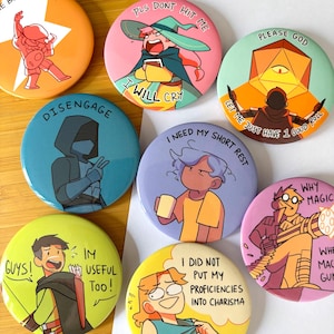 Könnte beinhalten: Eine Sammlung bunter runder Buttons mit Cartoon-Illustrationen und Text. Die Buttons zeigen verschiedene Charaktere und Sätze wie "Disengage", "I Need My Short Rest" und "Please God". Die Designs umfassen einen Zauberer, einen Schurken und andere Fantasy-Figuren.