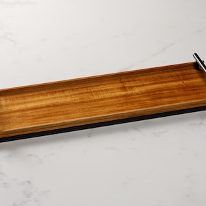 May include: A rectangular wooden serving tray with black metal handles. The tray has a natural wood finish and a black border.