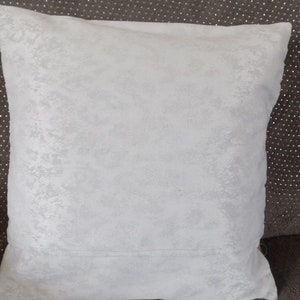May include: A white, soft, textured throw pillow with a subtle sheen. The pillow is square and has a simple design.