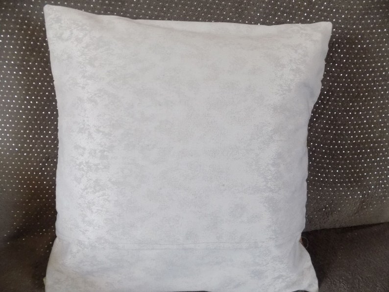 May include: A white, soft, textured throw pillow with a subtle sheen. The pillow is square and has a simple design.