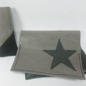 May include: A grey leather wallet with a black star design. The wallet is folded in half and has a separate grey leather pouch.