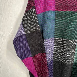 May include: A colorful sweater with a checkerboard pattern. The sweater features squares of black, purple, pink, green, and blue. The sweater has a black ribbed collar and a textured knit design.