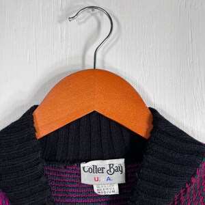 May include: A medium-sized sweater with a black collar and a pattern of pink, green, and blue geometric shapes. The label reads "Colter Bay U.S.A."