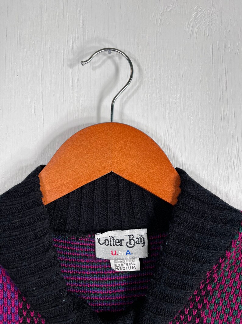 May include: A medium-sized sweater with a black collar and a pattern of pink, green, and blue geometric shapes. The label reads "Colter Bay U.S.A."