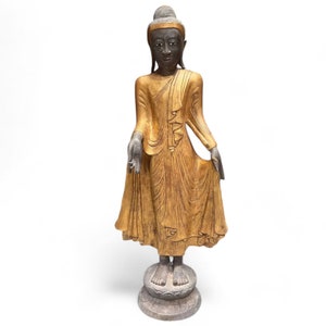 May include: A gold-painted standing Buddha statue with a black face and hands. The statue is on a stone base.