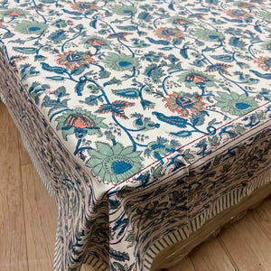 Könnte beinhalten: Ein weißes Tischtuch mit einem Blumenmuster in Blau-, Türkis- und Koralltönen. Das Design zeigt große Blumen und Blätter mit einem gestreiften Rand. Das Tischtuch ist über eine Oberfläche gefaltet.