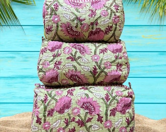 Pode incluir: Três nécessaires acolchoadas retangulares empilhadas. As bolsas apresentam um fundo verde claro com um padrão floral repetido em rosa e verde escuro. As bolsas estão sobre uma superfície arenosa com um fundo azul.