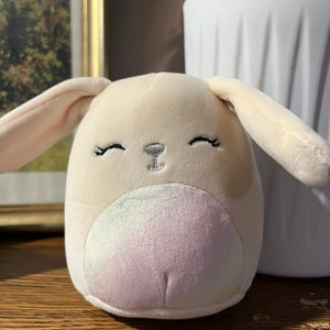 Puede incluir: Un juguete de peluche de conejo con un cuerpo marr&oacute;n claro, una cara blanca y una barriga de color arco&iacute;ris. El conejo tiene ojos y nariz bordados.