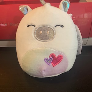 May include: White plush unicorn with a silver horn and hooves. The unicorn has a pink and purple heart on its belly.